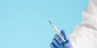 Hand in a blue glove holding syringe on blue