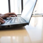 person using black laptop on brown table