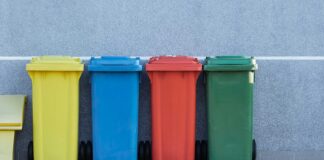 four assorted-color trash bins beside gray wall