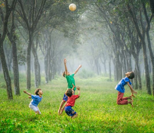 four boy playing ball on green grass