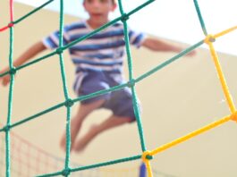 boy in blue and white striped shirt climbing on yellow metal fence