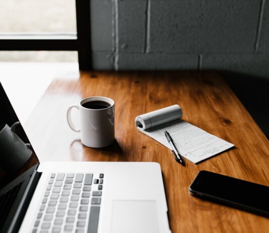 MacBook Pro, white ceramic mug,and black smartphone on table